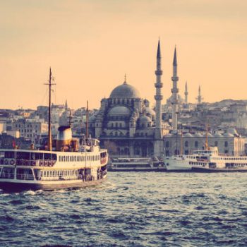 Cityscape of Istanbul at sunset - old mosque and turkish steamboats, view on Golden Horn. Muslim architecture and water transport in Turkey - touristic landmarks from sea voyage on Bosphorus.